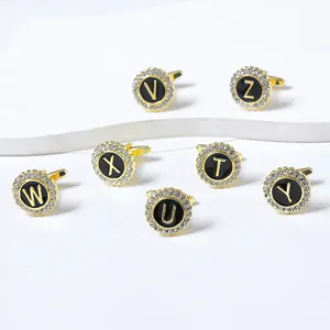 Detail view of round gold cufflinks with black letter centers and sparkling crystals