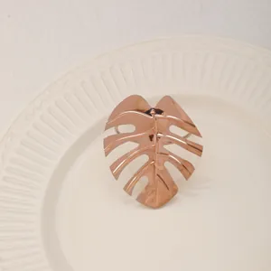 Detalle de servilletero de hoja de monstera oro rosa con vetas sobre plato blanco