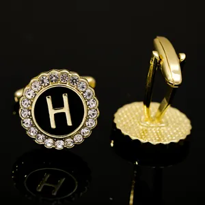 Macro view of gold cufflinks with black H letter inlay and sparkling crystal border