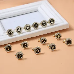 Detail of gold cufflinks with black round face, letter engravings, and white rhinestones