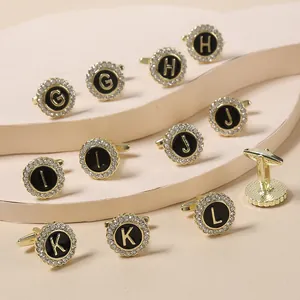 Close-up of gold-plated cufflinks with black enamel, crystal halo, and gold initial letters