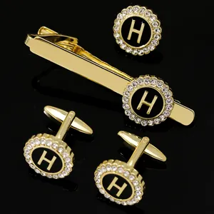 Close-up of gold tie clip and round H letter cufflinks with black inlay and crystals