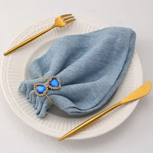 Detail of a gold heart napkin ring with blue stones on a white dinner plate