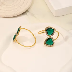 Close-up of heart-shaped gold earrings with emerald green stones on a white tray