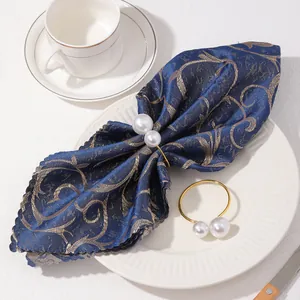 Primer plano de servilletero dorado con perlas dobles sobre elegante servilleta azul
