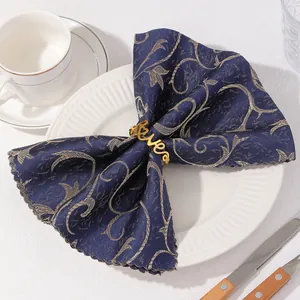 Rond de serviette Love doré sur tissu bleu à motifs posé sur une assiette blanche