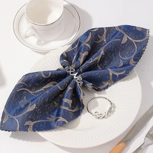 Détail de deux ronds de serviette Love argentés sur un tissu jacquard bleu marine