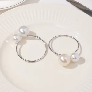 Detalle de elegantes servilleteros plateados con doble perla sobre un plato blanco
