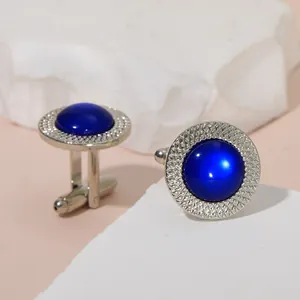 Close-up of silver-toned cufflinks with dark blue gemstone inlay and textured metal edges