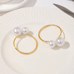 Detalle de servilleteros dorados con doble perla sobre un plato de cerámica blanca