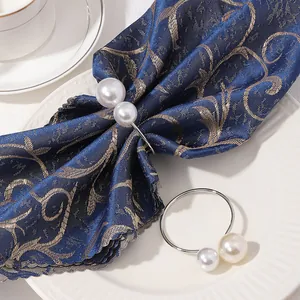 Detalle de servilleteros de plata con perlas blancas dobles sobre tela jacquard azul
