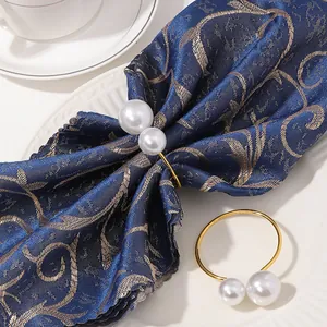 Primer plano de servilleteros dorados con doble perla sobre tela azul y plato de porcelana