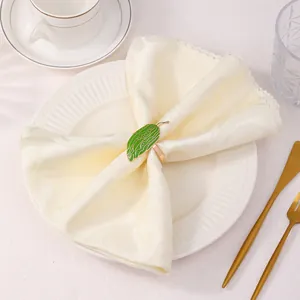 Dettaglio portatovagliolo in smalto verde su tessuto beige con posate dorate