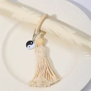 Rustic wood bead napkin ring with cotton tassel and Yin Yang charm on a plate