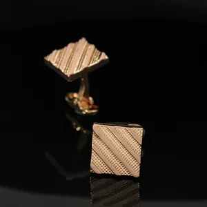 Macro detail of square striped gold and pink enamel cufflinks on black mirror surface