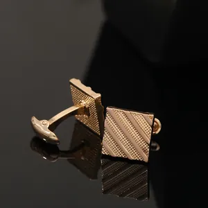 Macro shot of square gold cufflinks with diagonal stripes on a reflective surface