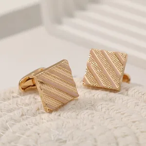 Detailed macro view of square gold cufflinks with pink enamel stripes on a woven texture