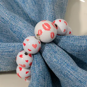 White wood bead napkin ring with red heart and lip prints on a blue textured fabric
