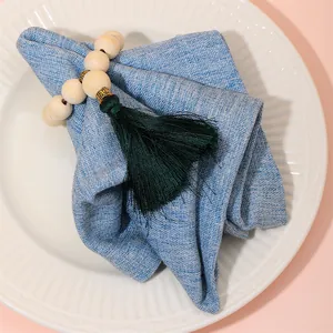 Close-up of bohemian wood bead napkin ring with deep green tassel on a blue linen napkin