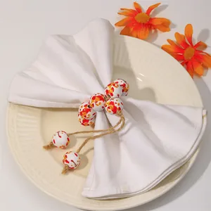 Close-up of Autumn wood bead napkin ring with orange maple leaf pattern and rustic twine tassel
