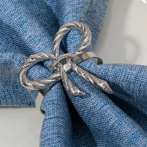 Elegante servilletero de lazo plateado con diseño de cuerda sobre tela azul y plato blanco