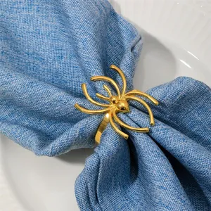 Détail d'un rond de serviette araignée dorée posé sur une serviette en lin bleu chic