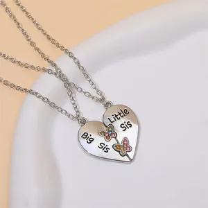 Détail des colliers cœur Big Sis et Little Sis avec papillon en strass coloré dans un bol