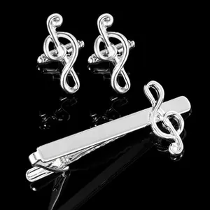 Polished silver musical note cufflinks and tie clip set on a black reflective background
