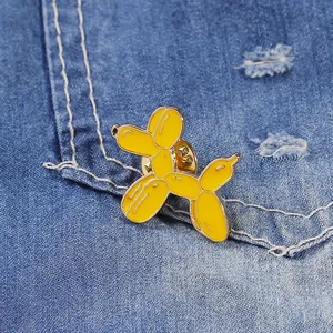 Primo piano della spilla smaltata a forma di cane palloncino giallo su tessuto denim blu