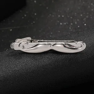 Detailed close-up of a silver mustache shaped metal tie clip on a black textured surface