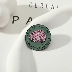 Dettaglio di una spilla smaltata con cervello rosa e testo sulla salute mentale su vassoio