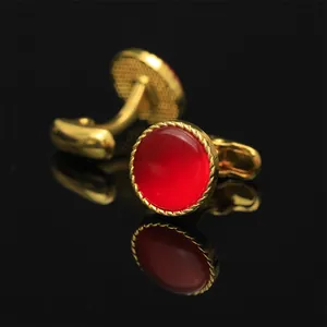 Detalle de gemelos dorados con piedra roja y borde de cuerda trenzada sobre fondo de espejo