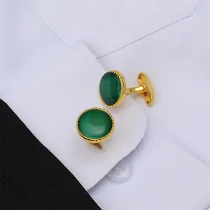 Primer plano detallado de gemelos redondos dorados con piedra verde en camisa blanca