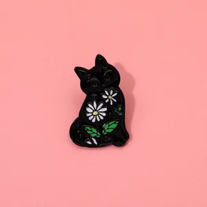 Close-up of black enamel cat brooch with white daisy patterns and green leaves