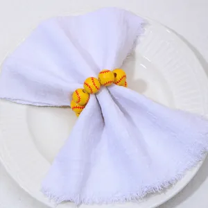 Détail d'un rond de serviette en bois jaune motif softball sur une serviette en lin blanc