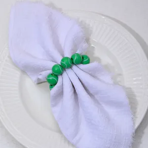 Détail de ronds de serviette en perles de tennis vert sur une serviette blanche et plat