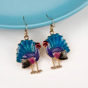 Close-up of colorful enamel turkey drop earrings hanging on a blue ceramic dish