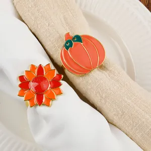 Detail of enamel pumpkin and sunflower napkin rings with gold trim on fabric napkins