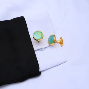 Detail of round gold cufflinks with gradient turquoise stone on a white shirt sleeve