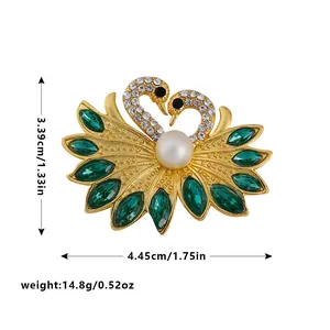 Elegant gold-tone swan brooch with green crystals and white pearl, size measurements shown