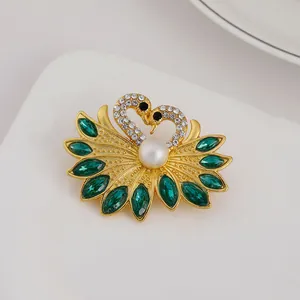 Detailed close-up of golden swan brooch with green gemstones and white pearl accent
