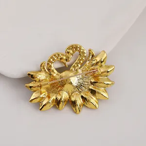 Detail of golden twin swan heart brooch featuring secure safety pin and alloy base