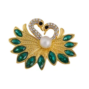 Elegant twin swan brooch featuring emerald green crystals and a white pearl accent