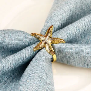 Detalle de servilletero de estrella de mar dorada con diamantes en servilleta de lino azul