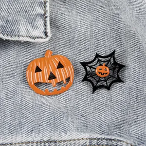 Detail of Halloween pumpkin and spider web brooch set pinned on light blue denim fabric