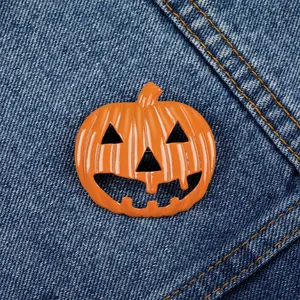 Close-up of bright orange pumpkin brooch with cut-out details on blue denim fabric