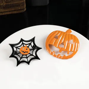 Halloween brooch set with orange pumpkin and black spider web pins on a ceramic plate