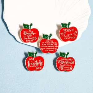 Detailed view of red enamel apple brooches with gold edges and teacher appreciation quotes