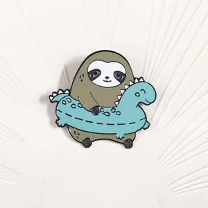 Creative enamel pin featuring a cute sloth with a blue dinosaur swimming ring on white