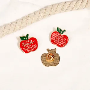 Detail of red apple enamel pins with inspirational teacher quotes on white fabric background